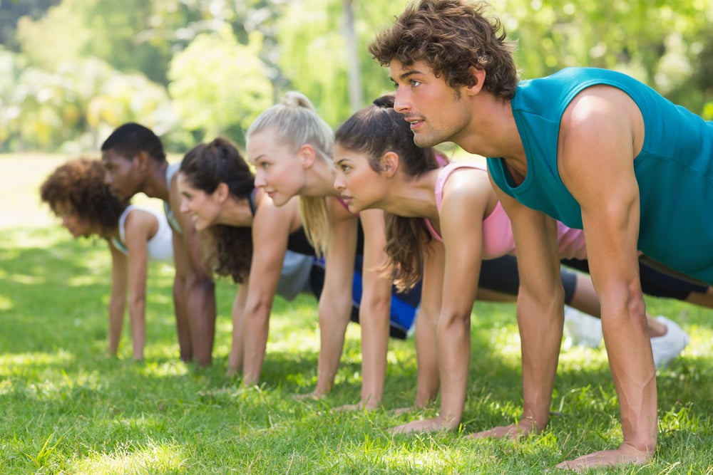 Side view of a group of fitness people doing push ups in the park